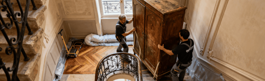 Débarrasseurs transportant meuble volumineux escalier colimaçon immeuble haussmannien, protections murales installées