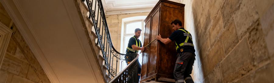 Débarrasseurs transportant meuble volumineux escalier colimaçon immeuble parisien ancien, manutention difficile