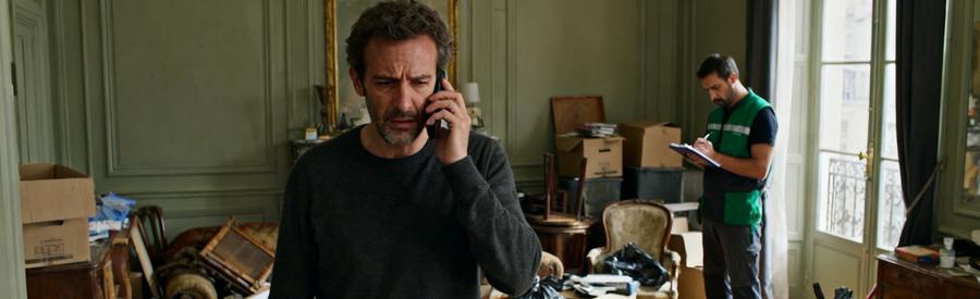 Particulier pressé au téléphone dans un salon encombré, professionnel du débarras évaluant la situation.