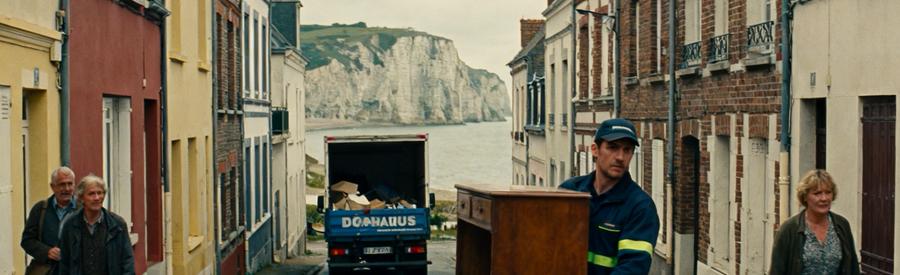 Professionnel du débarras portant un meuble dans le quartier étroit du Pollet à Dieppe, avec la falaise en arrière-plan.