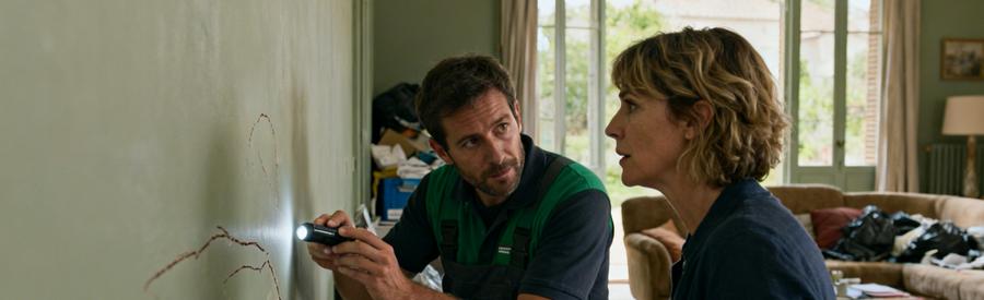 Un professionnel évalue un mur tout en discutant de l'assurance avec un client dans un espace de vie.