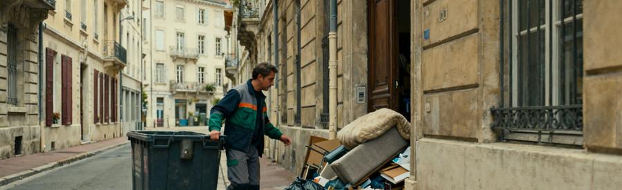 Professionnel du débarras naviguant dans les ruelles d'Aix-les-Bains, entouré d'immeubles haussmanniens et d'objets à évacuer.