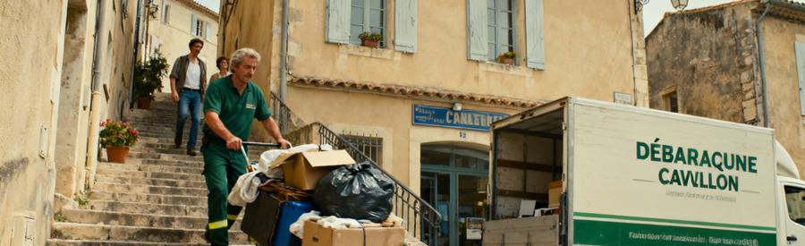 Un professionnel du débarras monte des escaliers étroits à Cavaillon, avec des objets à évacuer et un camion en attente.