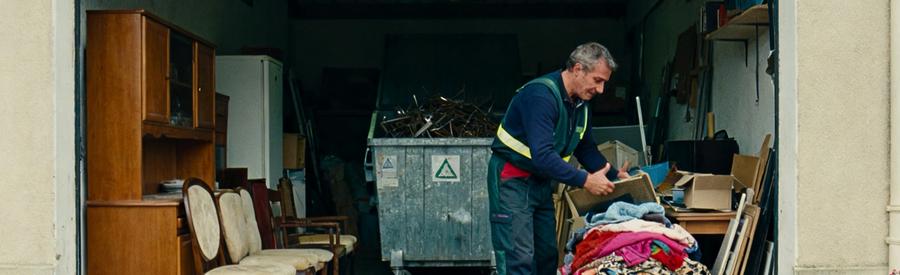 Débarrasseur triant des objets dans un garage, avec textiles, meubles et ferraille pour recyclage à Berre-l'Étang.