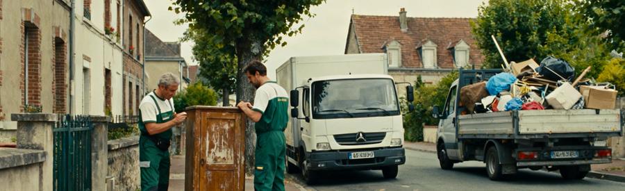 Deux professionnels du débarras discutent d'un meuble sur le trottoir dans une rue des Ardennes, montrant des différences de services.